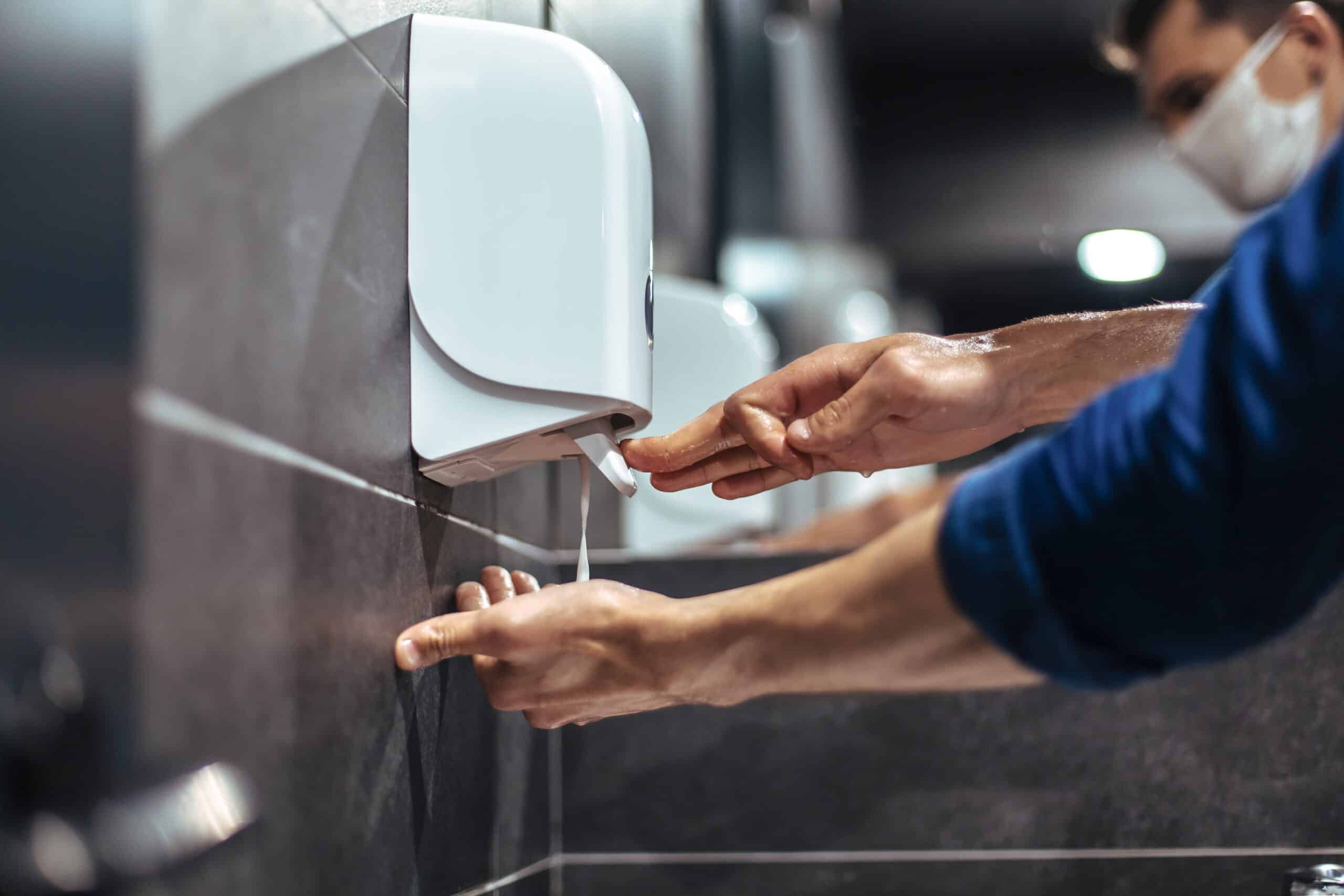 person using hand sanitiser dispenser provided by Excel Hygiene